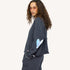 Side view of a woman wearing a charcoal sweatshirt with an paint splat heart elbow patch and sunglasses.