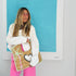 Model wearing a white paint-splattered denim jacket and pink pants, carrying a woven straw tote bag with a palm tree and heart appliqué design. Handpainted by Kerri Rosenthal