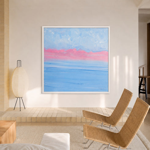 A square framed abstract painting hanging on a beige wall in a modern room. The artwork features a soft blue sky with a vibrant pink horizon and horizontal blue bands below.