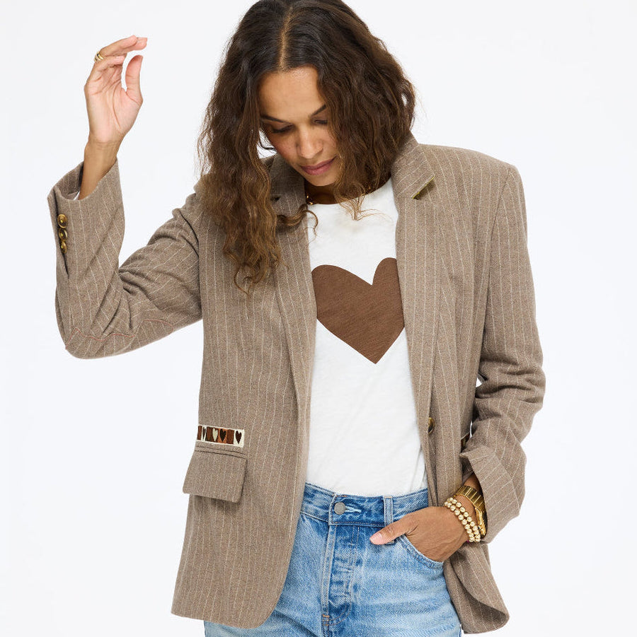 Model wearing the Workday Love Brigade Blazer in taupe over the Long Sleeve Suke Imperfect Heart Tee in cream with a brown heart and jeans, one hand raised