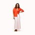 Woman wearing a tomato cardigan with a gold jewelery, natural white drawstring pants, and tomato heels.
