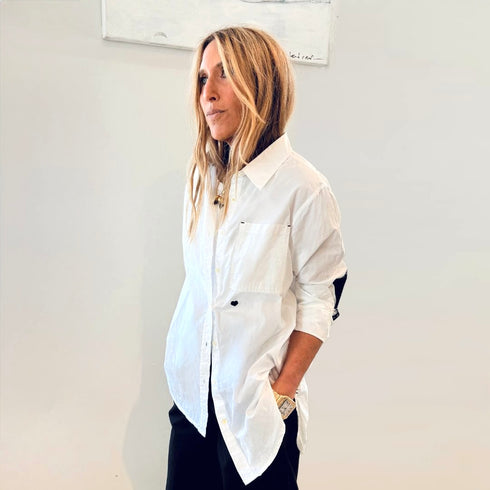 Woman wearing a white shirt with rolled-up sleeves against a plain background