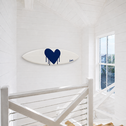 Kerri Rosenthal navy heart surfboard mounted horizontally on a wall near a staircase landing