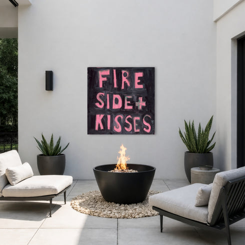 Kerri Rosenthal "Fireside + Kisses" pink word art painting displayed on outdoor patio wall above modern fire pit, black and pink typography canvas art styled with neutral outdoor furniture and potted plants