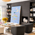 A modern living room featuring a large, colorful abstract canvas painting leaning against a dark gray wood-paneled wall. The room is styled with a cream sectional sofa, two dark gray armchairs, a light wood coffee table, and built-in black shelving.