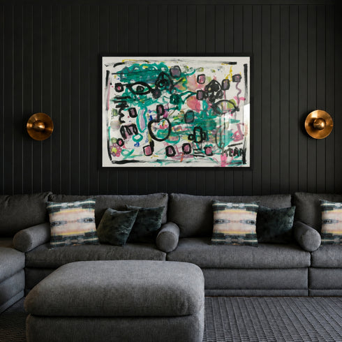 Black framed abstract painting by Kerri Rosenthal with teal, black and pink heart motifs displayed above gray sectional sofa in moody dark living room