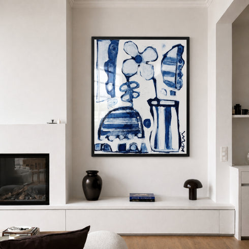 Black-framed blue and white abstract floral painting hanging above a built-in shelf with a dark ceramic vase and mushroom lamp, beside a fireplace in a minimalist living room.