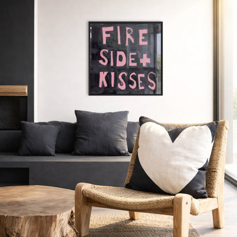 Kerri Rosenthal "Fireside + Kisses" painting in black frame displayed in boho-modern living room with woven chair, heart pillow, and live-edge wood