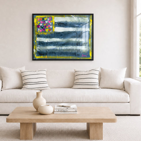Living room with a white sofa, wooden coffee table, and Abstract Flag painting with blue, white, and multicolored heart design on a white background. Artwork by Kerri Rosenthal.