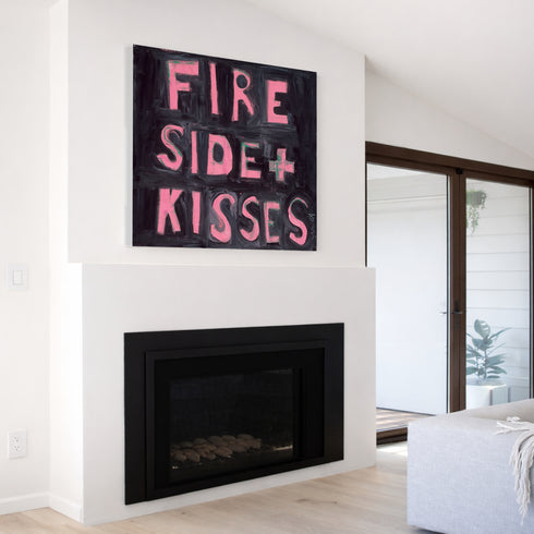 Kerri Rosenthal "Fireside + Kisses" pink word art painting displayed above modern white fireplace, black and pink typography canvas art in contemporary living room