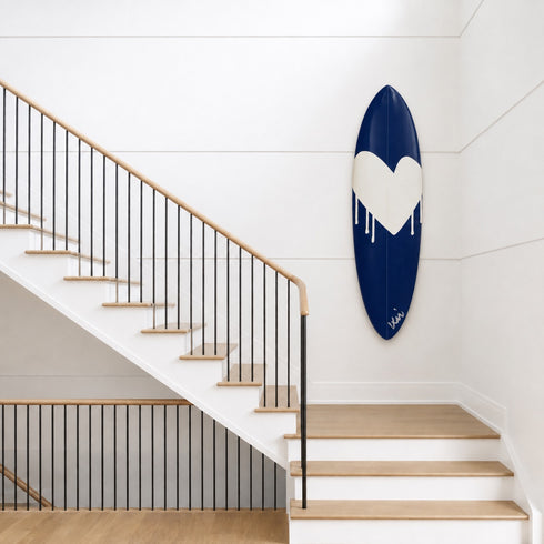 Kerri Rosenthal navy heart surfboard displayed on a wall above a wooden staircase