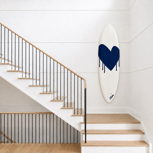 Kerri Rosenthal navy heart surfboard displayed on a wall above a wooden staircase