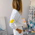 Person wearing a white outfit with yellow elbow patches in an art studio.