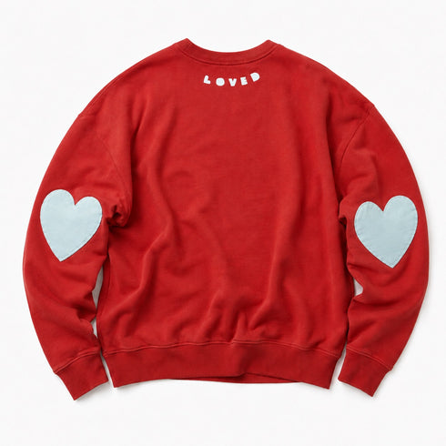 A red crewneck sweatshirt shown from the back, featuring a small white 'LOVED' text print at the center of the neck and two light blue heart patches on each sleeve, laid flat against a white background.