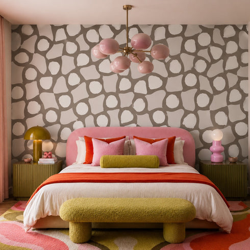 Modern bedroom with patterned wallpaper, colorful bedding, and a pink chandelier.