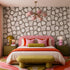 Modern bedroom with patterned wallpaper, colorful bedding, and a pink chandelier.