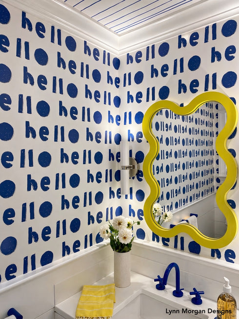 Bathroom with blue 'hello' wallpaper, yellow mirror, and white sink.