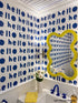 Bathroom with blue 'hello' wallpaper, yellow mirror, and white sink.