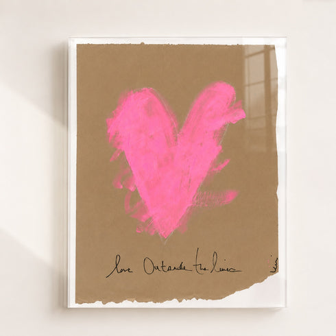 A framed art print featuring a textured bright pink heart on a brown kraft paper background, with a white frame and a signature at the bottom, displayed against a white wall.