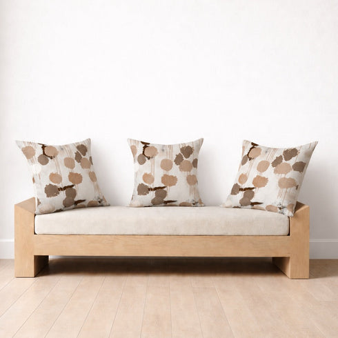 A light wood daybed with a cream upholstered seat cushion and three matching patterned throw pillows, set against a plain white wall on a light wood plank floor.