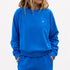 Woman wearing a blue crewneck sweatshirt with a small heart logo and matching sweatpants.