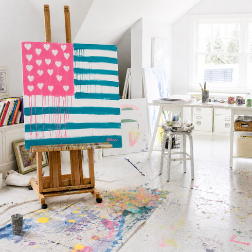 Kerri Rosenthal's Sunshine Saltwater Forever Flag original painting displayed on a wooden easel in the Kerri Rosenthal's bright, paint-splattered studio