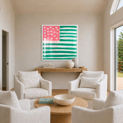 The Heart-Flag painting in pink and green, framed in white, displayed above a wooden console table in a neutral, light-filled living room with cream linen armchairs arranged around a round wooden coffee table. Painted by artist, Kerri Rosenthal.
