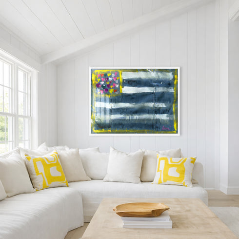 Living room with a white sofa, yellow pillows, and an Abstract Flag painting with blue, white, and multicolored heart design on a white background. Artwork by Kerri Rosenthal. White Frame.