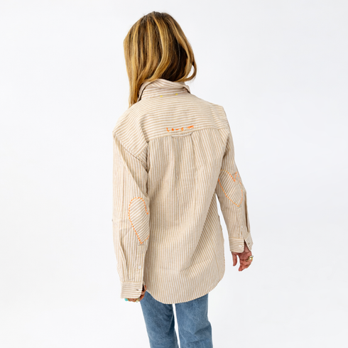 Woman wearing a beige striped shirt with a visible brand logo on a white background