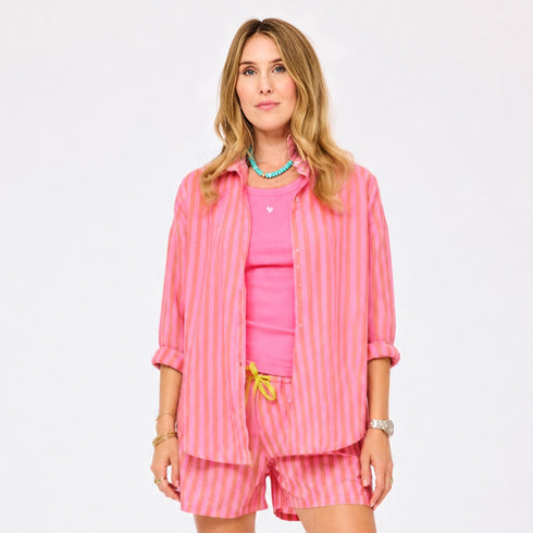 Woman wearing a pink and orange striped oversized button-down shirt with matching shorts, styled with a pink tank top, turquoise beaded necklace, and yellow drawstring detail.