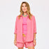 Woman wearing a pink and orange striped oversized button-down shirt with matching shorts, styled with a pink tank top, turquoise beaded necklace, and yellow drawstring detail.