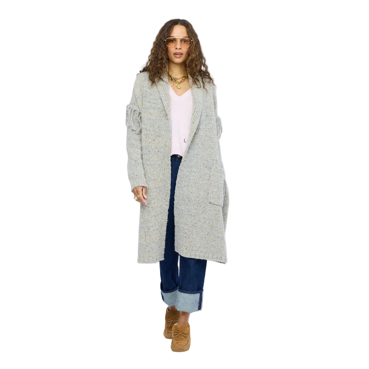Model walking in a long gray fringe cardigan layered over a white top and cuffed jeans, tan ankle boots, self-tie belt at the waist. Kerri Rosenthal women's sweaters