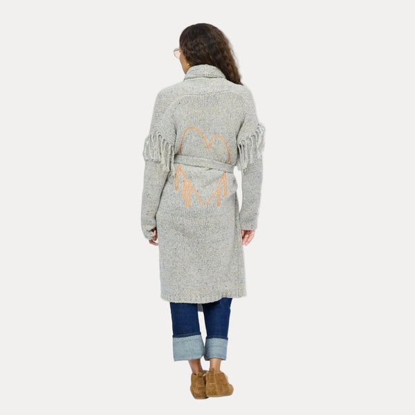 Back view of model wearing a long gray fringe cardigan with an orange open heart embroidered between the shoulder blades.