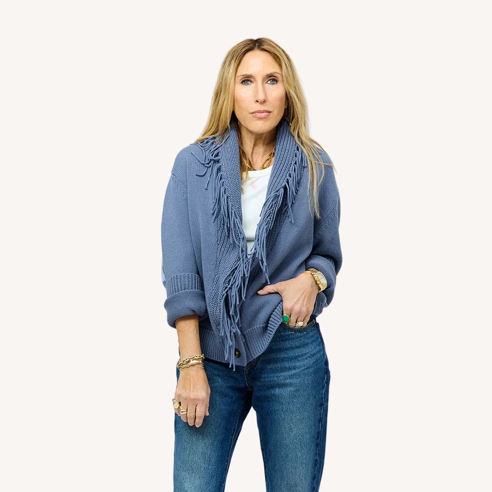 Woman wearing a Kerri Rosenthal slate blue fringe knit cardigan over a white top, styled with blue jeans and gold jewelry.