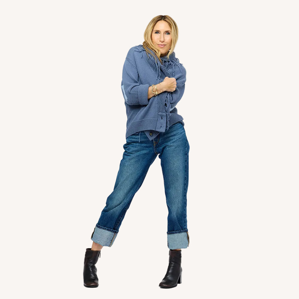 Woman wearing a Kerri Rosenthal slate blue fringe knit cardigan with the fringe collar pulled up, styled with cuffed blue jeans and black ankle boots.