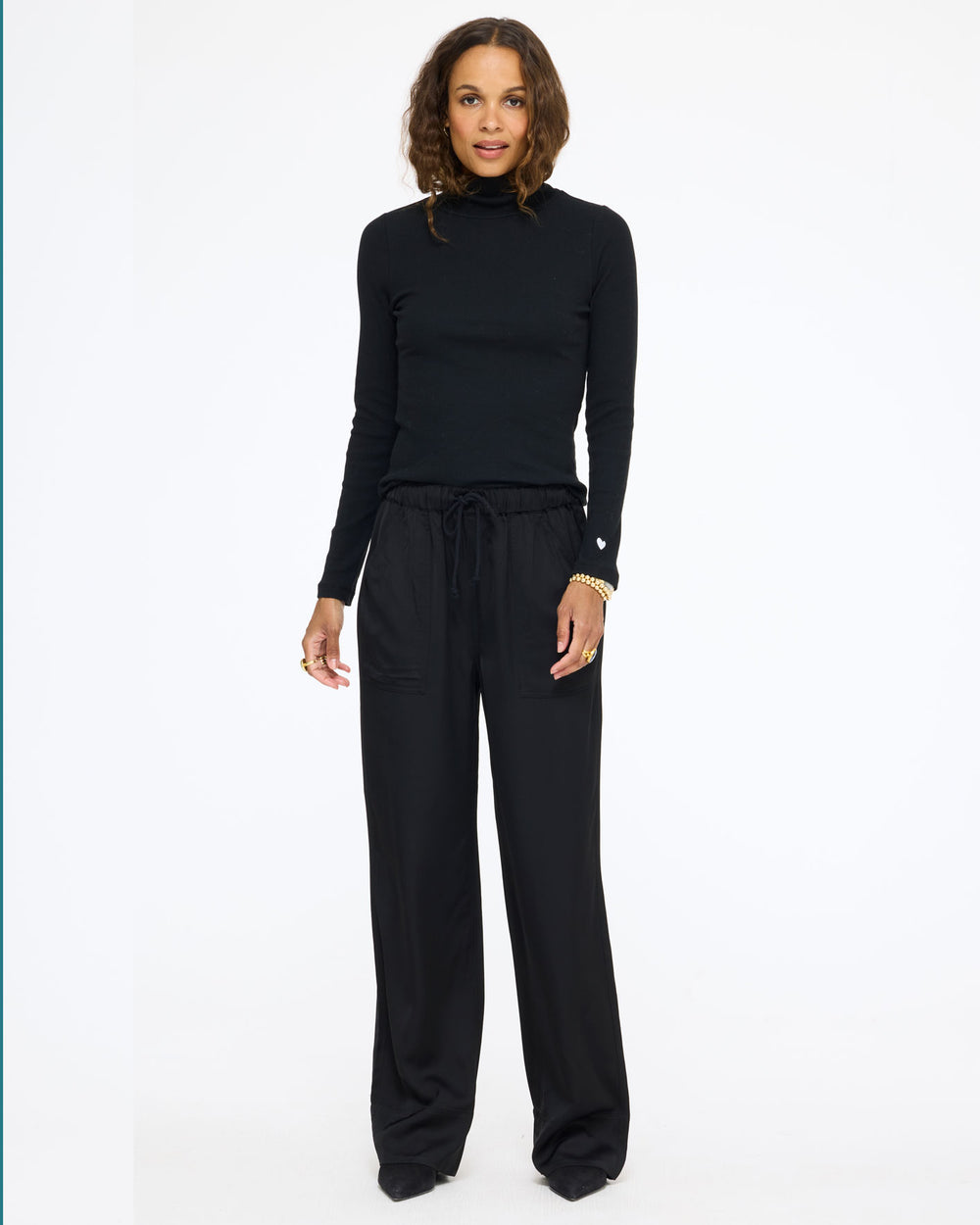 Model wearing the Mock Neck Rib Tee in black with the Coast Pant in black, full length front view