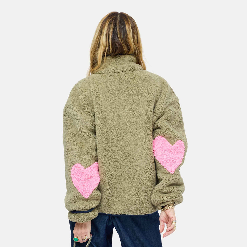 Back of model wearing olive sherpa jacket from behind, showing pink heart-shaped elbow patches and wide-leg denim jeans. Shop Kerri Rosenthal women's jackets.