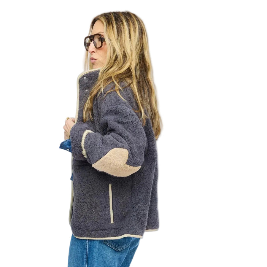 Side view of model wearing gray sherpa jacket with cream contrast trim, snap-button front, and cuffed denim jeans