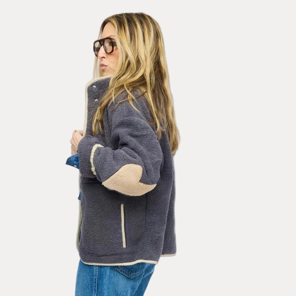 Side view of model wearing gray sherpa jacket with cream contrast trim, snap-button front, and cuffed denim jeans