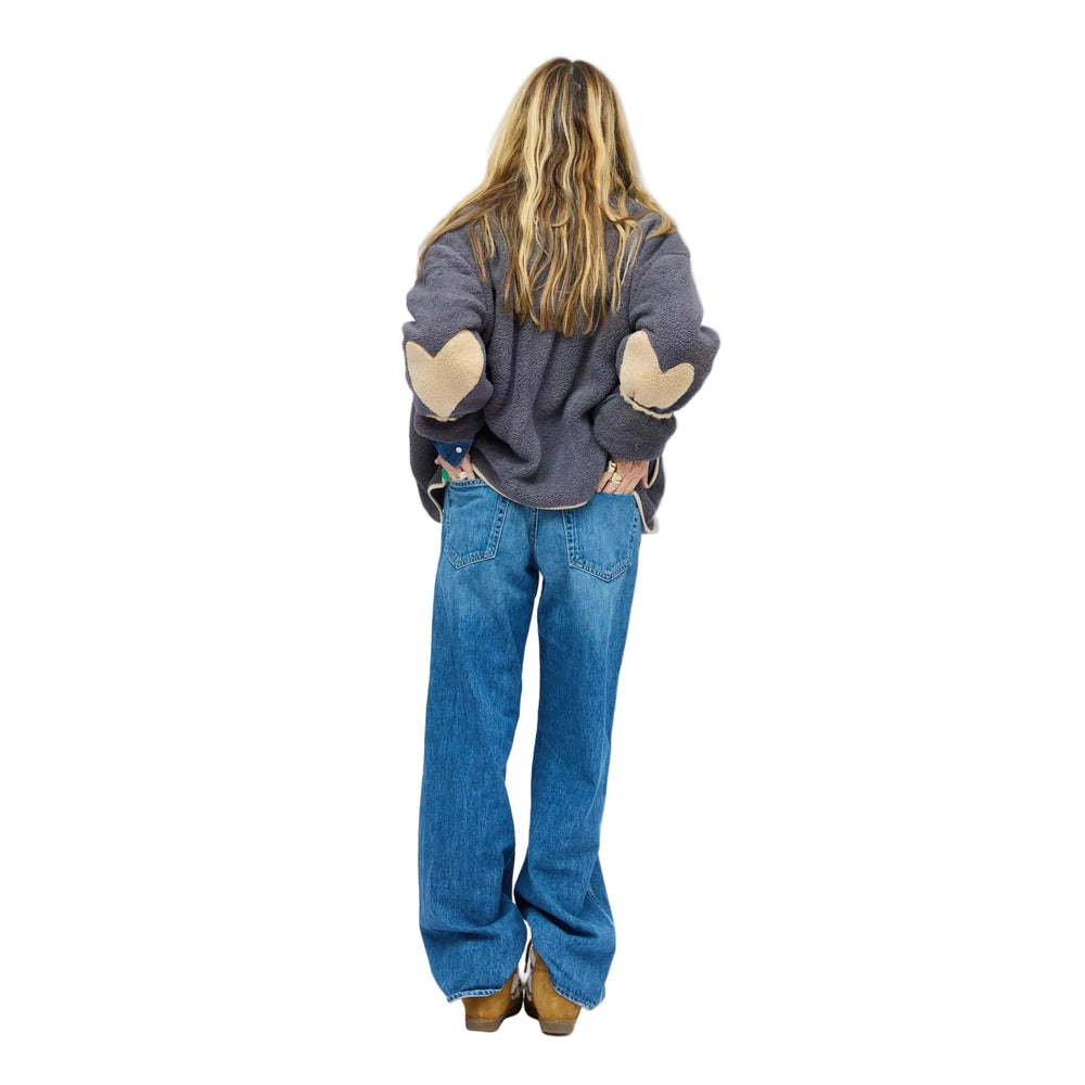 Model wearing olive sherpa jacket with navy contrast trim, snap-button front, and heart-print lining peeking from sleeve.