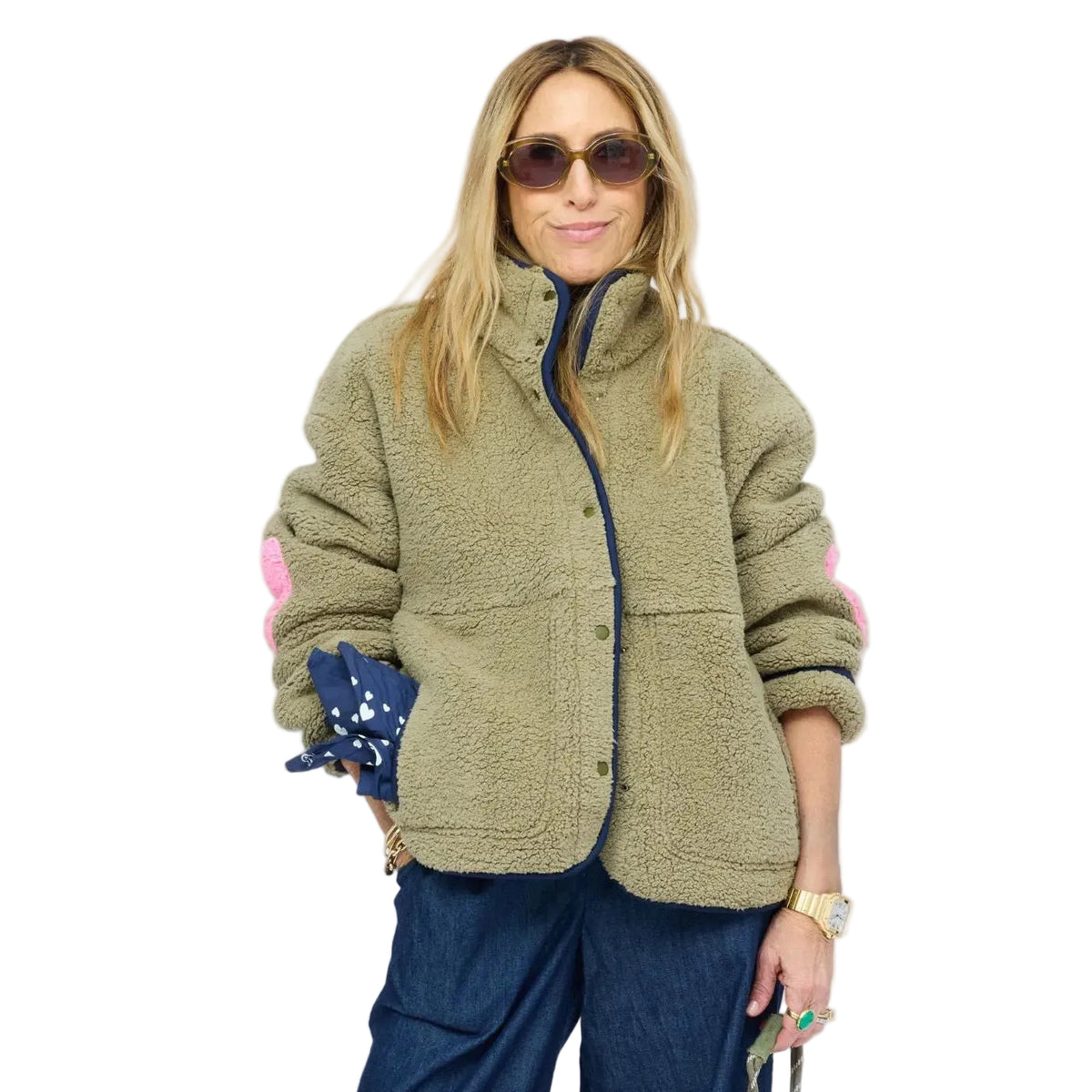 Model wearing olive sherpa jacket with navy contrast trim, snap-button front, and heart-print lining peeking from sleeve.