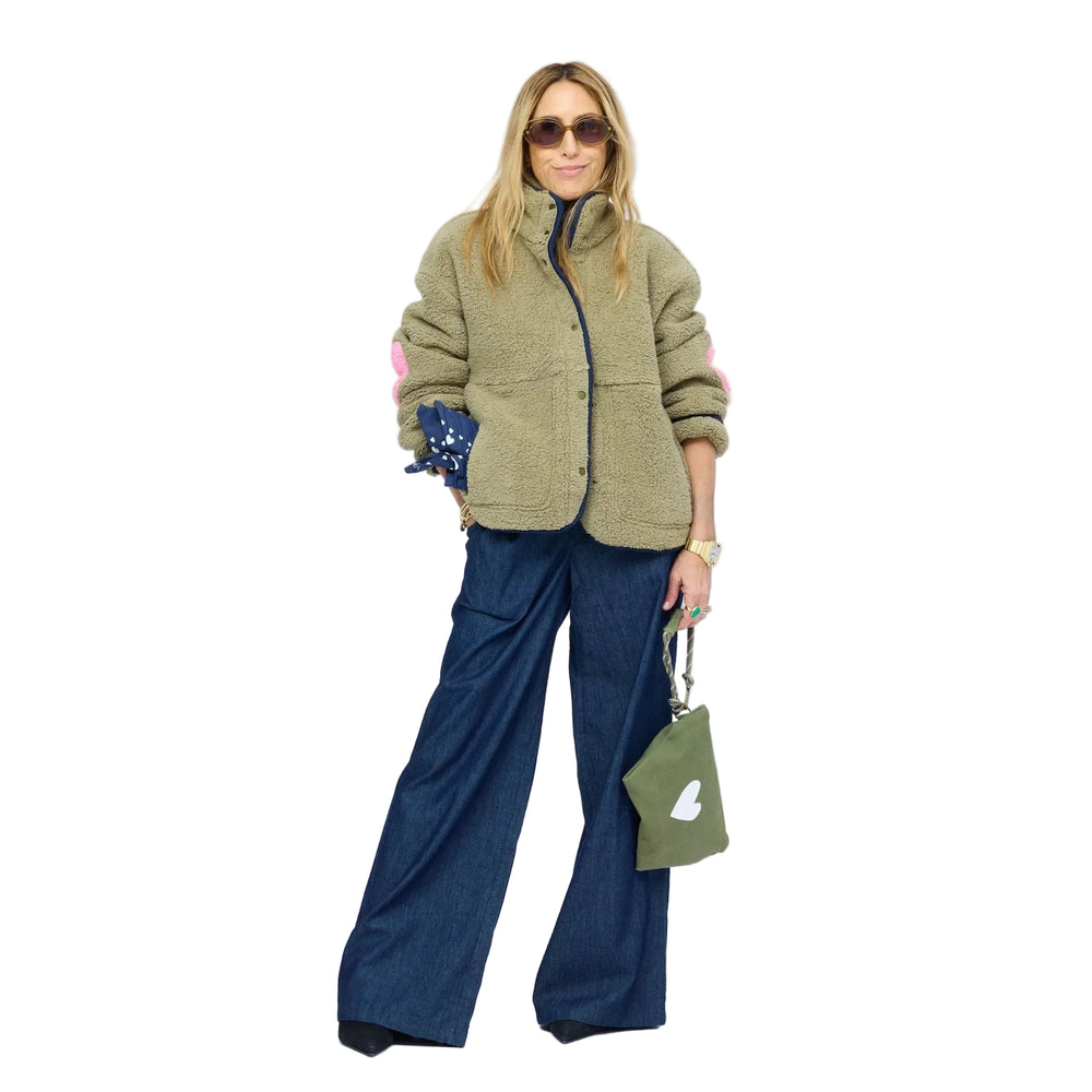 Model wearing olive sherpa jacket with navy contrast trim, snap-button front, and heart-print lining peeking from sleeve.