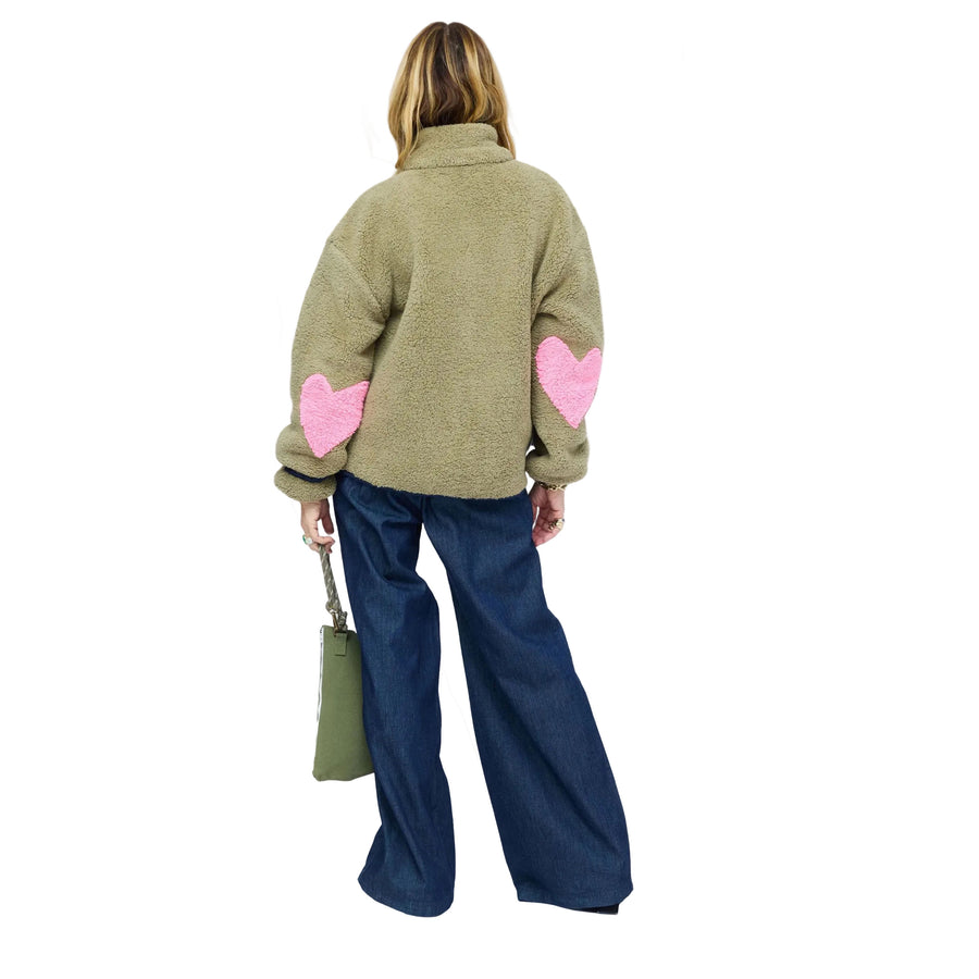 Back of model wearing olive sherpa jacket from behind, showing pink heart-shaped elbow patches and wide-leg denim jeans. Shop Kerri Rosenthal women's jackets.