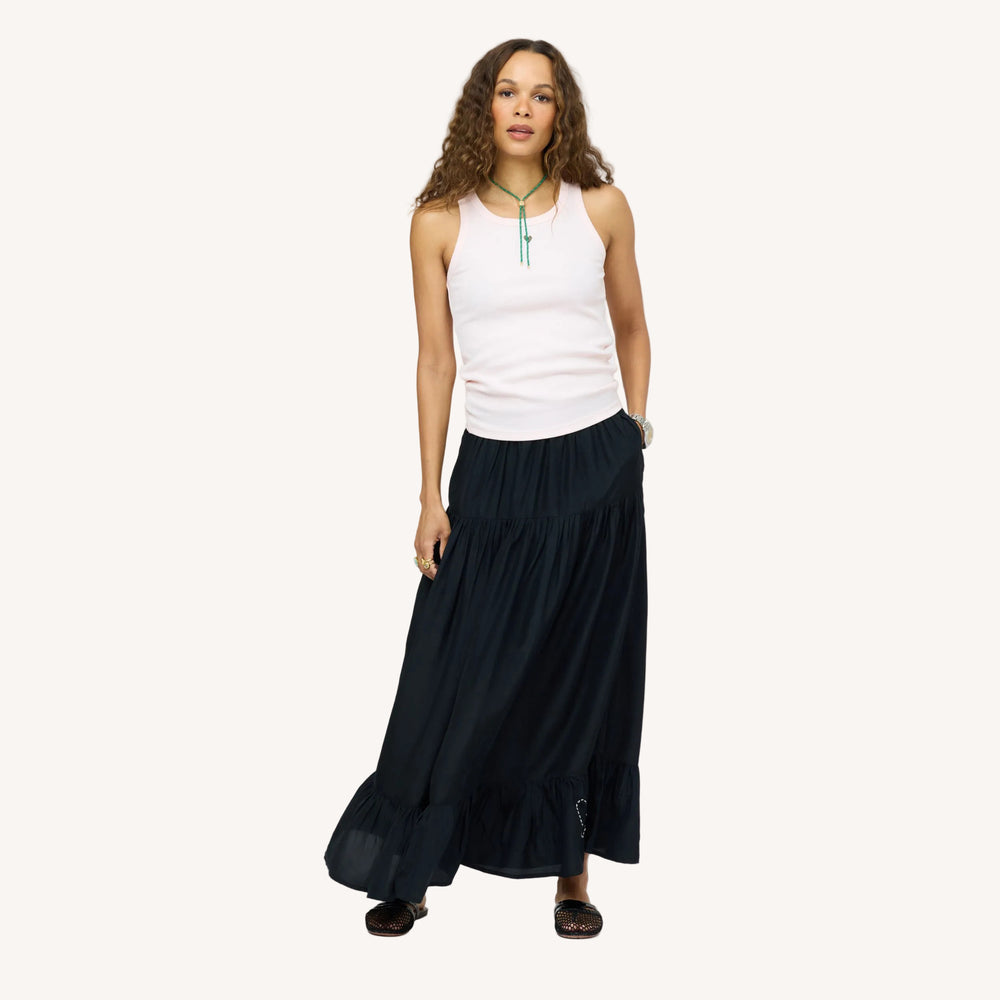 Model wearing a pale pink tank top with a turquoise beaded necklace and a black tiered maxi skirt, paired with woven black flats. Women's clothing by Kerri Rosenthal