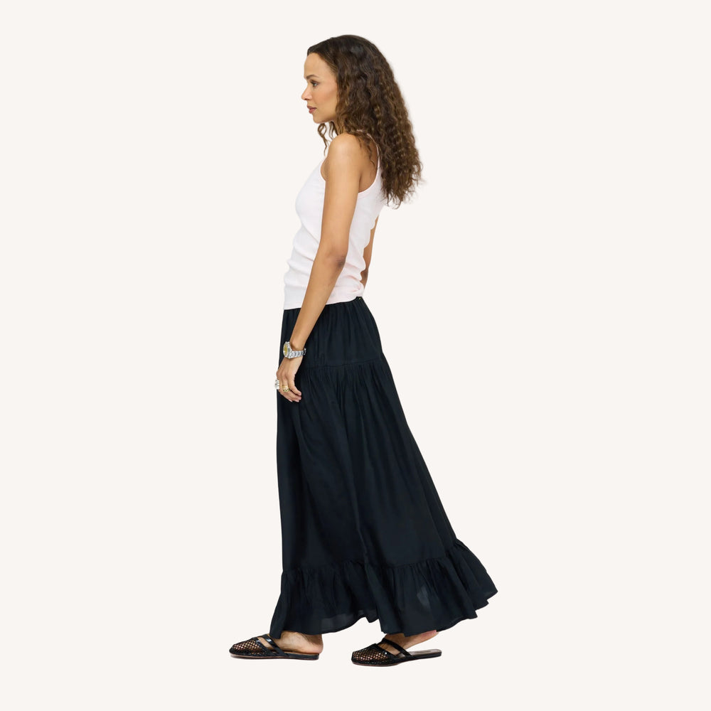 Side view of model wearing a pale pink tank top  and a black tiered maxi skirt, paired with woven black flats. Women's clothing by Kerri Rosenthal