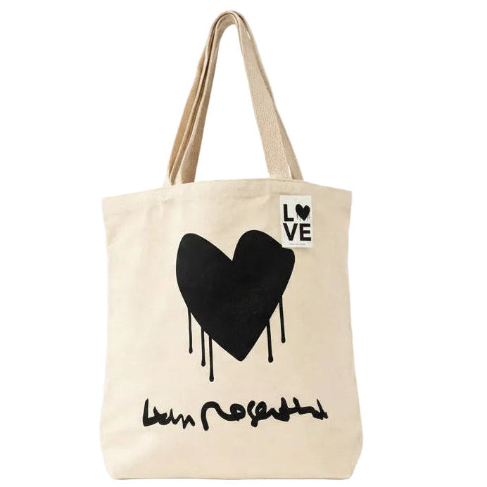 A cream-colored canvas tote bag with a black dripping heart graphic and the word 'LOVE' printed in a white square on the upper right side. The bag has two beige shoulder straps and a black script graphic underneath the heart.