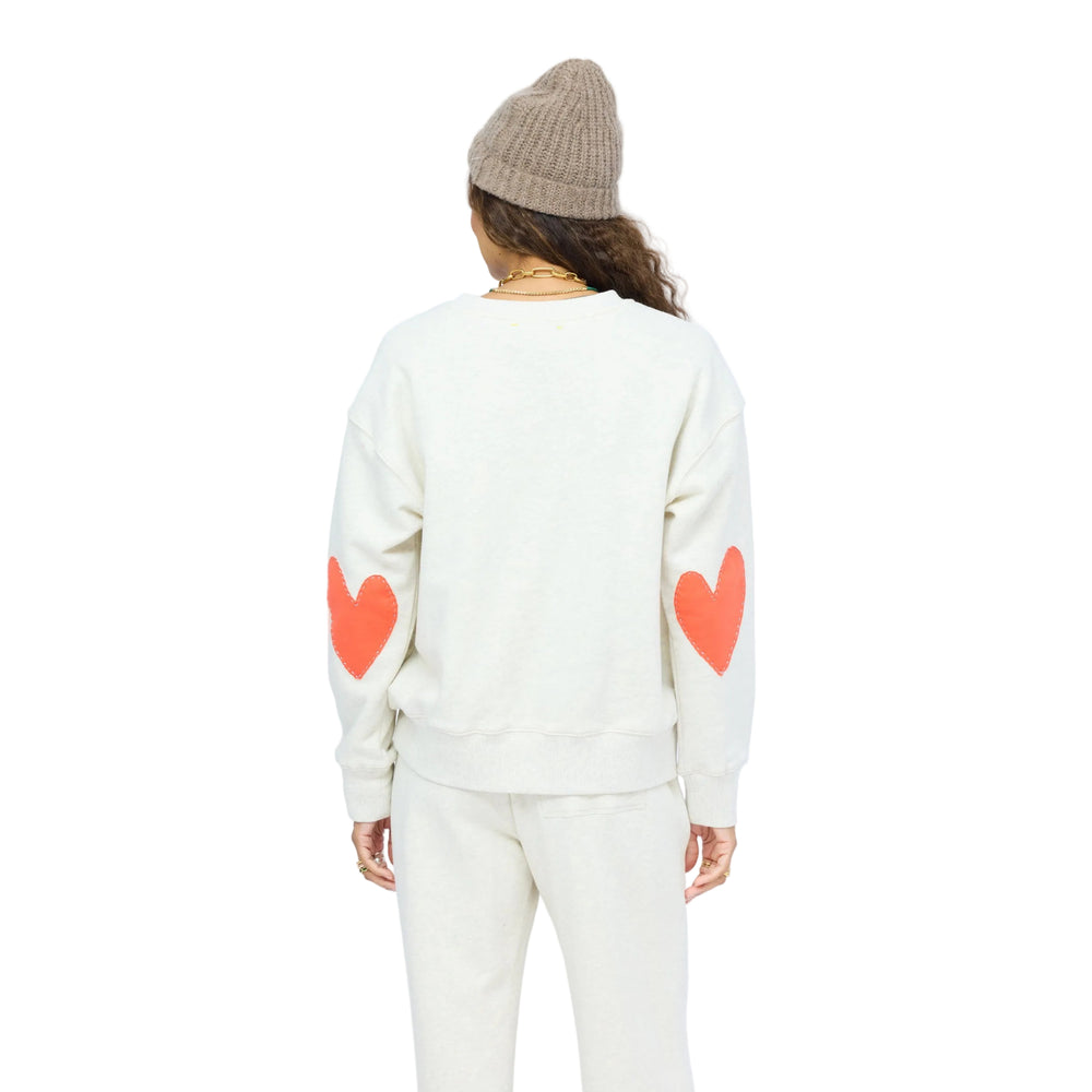 Back of woman wearing a Kerri Rosenthal oatmeal heather sweatshirt and matching wide-leg sweatpants, a taupe knit beanie, and layered gold jewelry.