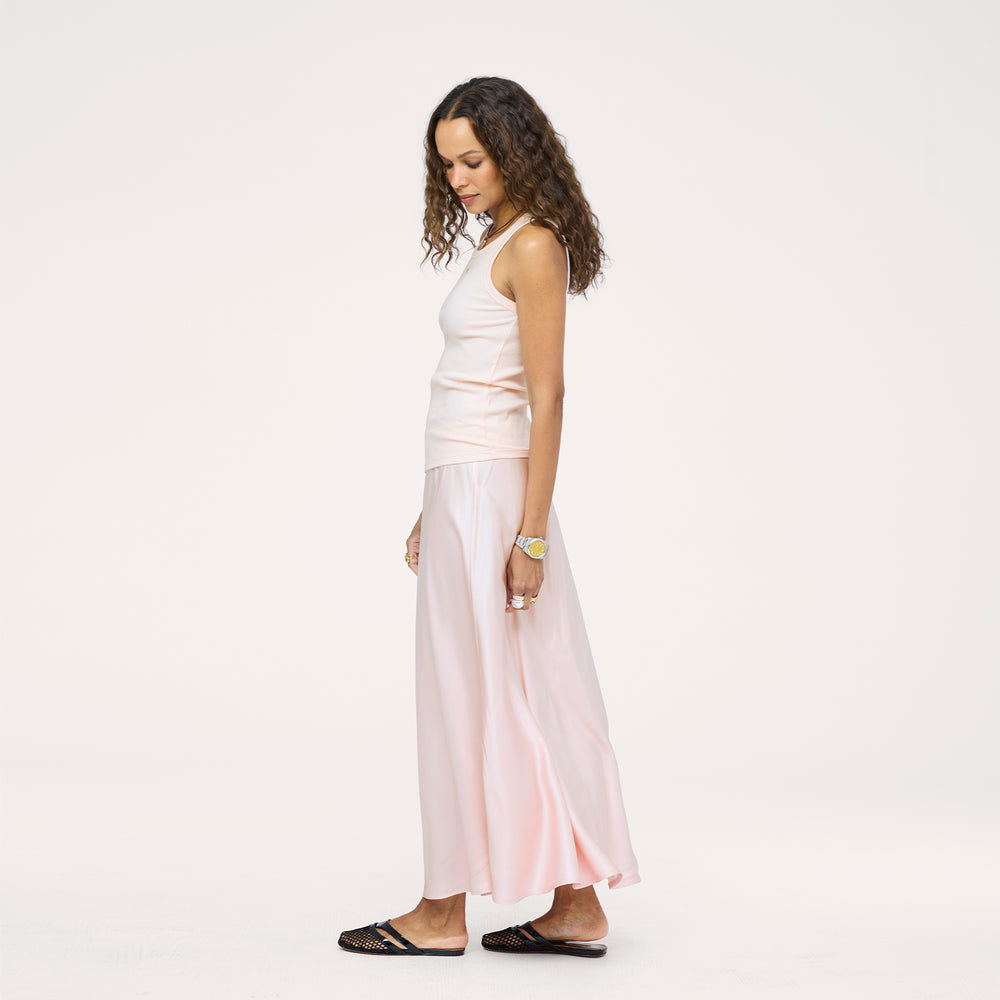 Side view of a model wearing a cropped pink button-down top with a flowy pink maxi skirt, barefoot