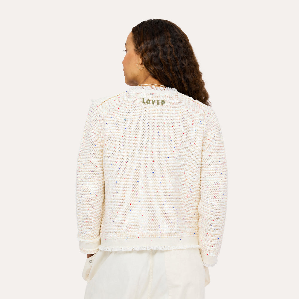 Back view of woman wearing a Kerri Rosenthal cream boucle tweed fringe jacket with white pants.