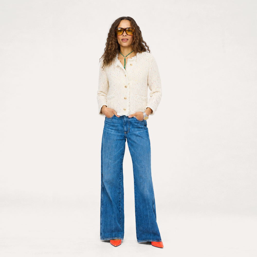Woman in Kerri Rosenthal cream tweed jacket styled with wide-leg jeans, orange heels, and sunglasses.